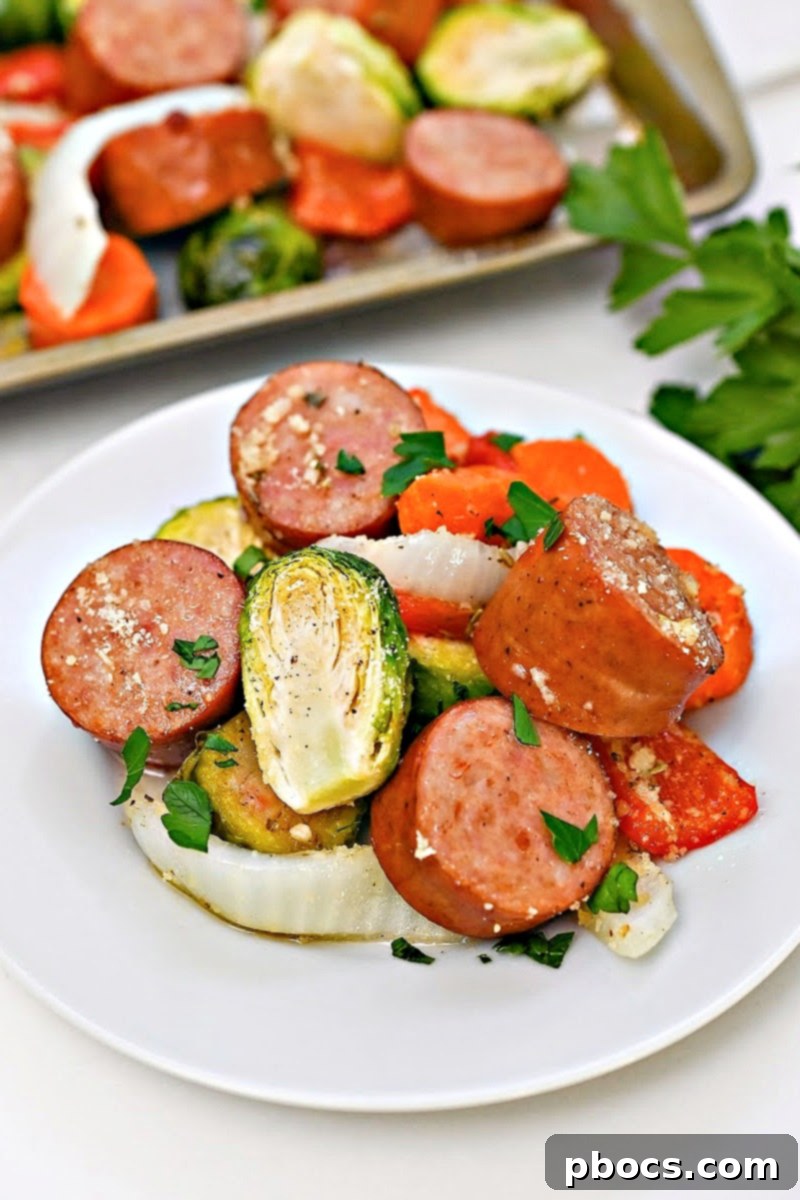 Low Carb Honey Garlic Sausage and Veggies on a white plate in front of a sheet pan of food, showcasing a vibrant and appealing meal.