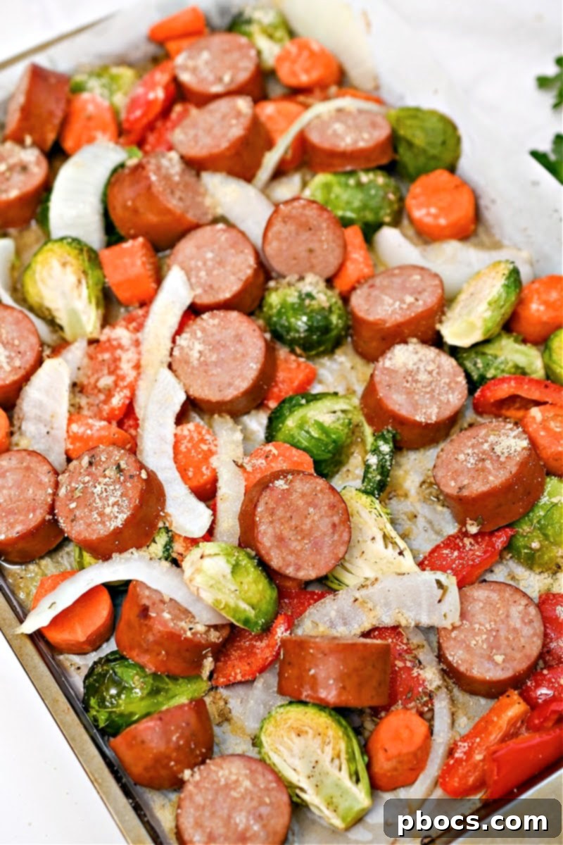 A full sheet pan laden with kielbasa sausages and a colorful assortment of low-carb vegetables, ready to be roasted.