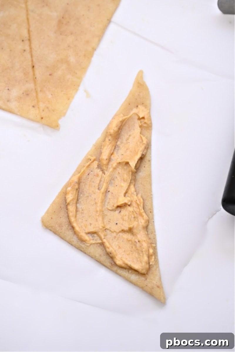 Carefully spreading pumpkin filling onto each dough triangle before rolling to create the crescent shape.