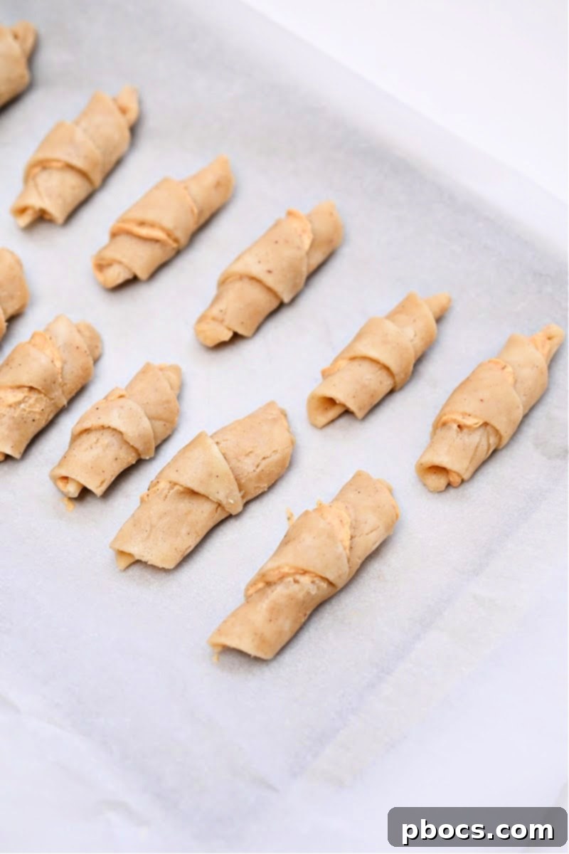 Unbaked keto pumpkin crescent rolls arranged on a parchment-lined baking sheet, ready for the oven.