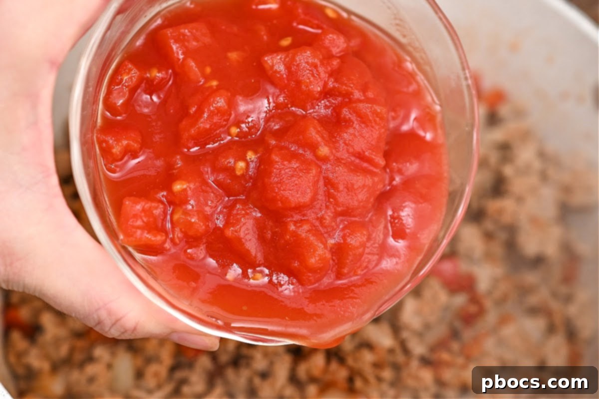 Diced tomatoes from a can being added to the chili mixture