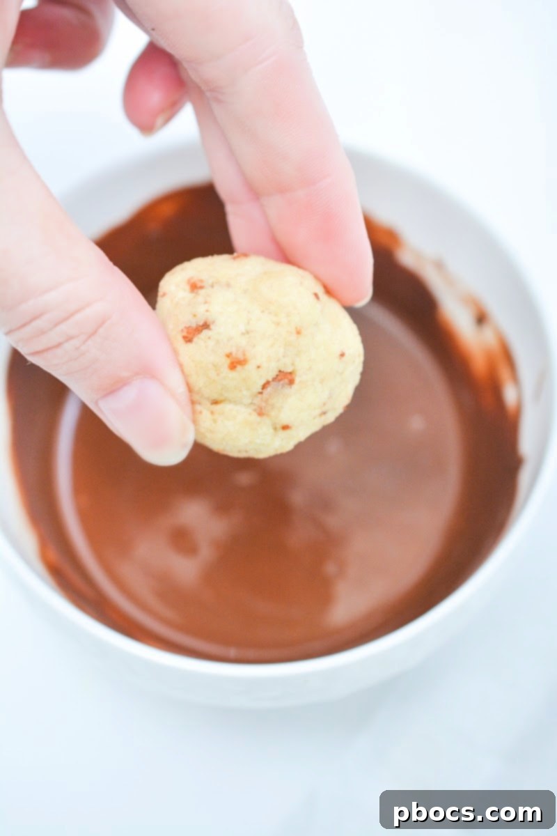 A chilled maple bacon bite being dipped halfway into melted chocolate.