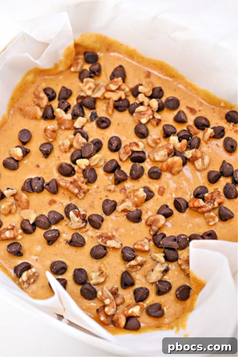 The fudge mixture spread in a parchment-lined baking dish with toppings