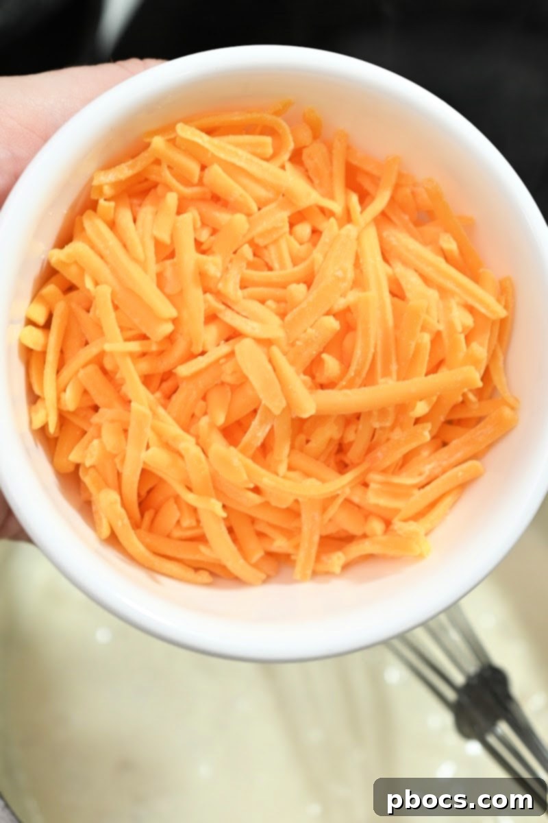Shredded cheddar cheese being added to the sauce