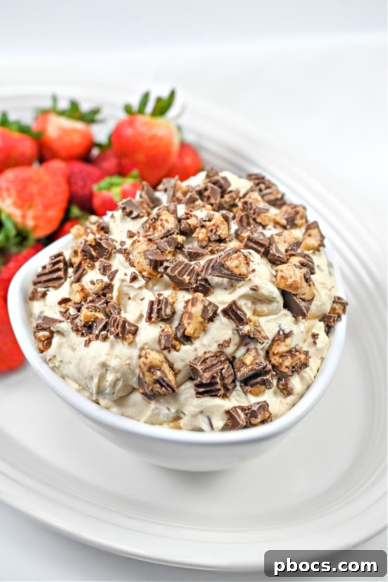 Keto Peanut Butter Chocolate Dip 2 Creamy Keto Reese's Dip in a white bowl with chopped keto peanut butter cups and strawberries, viewed from above