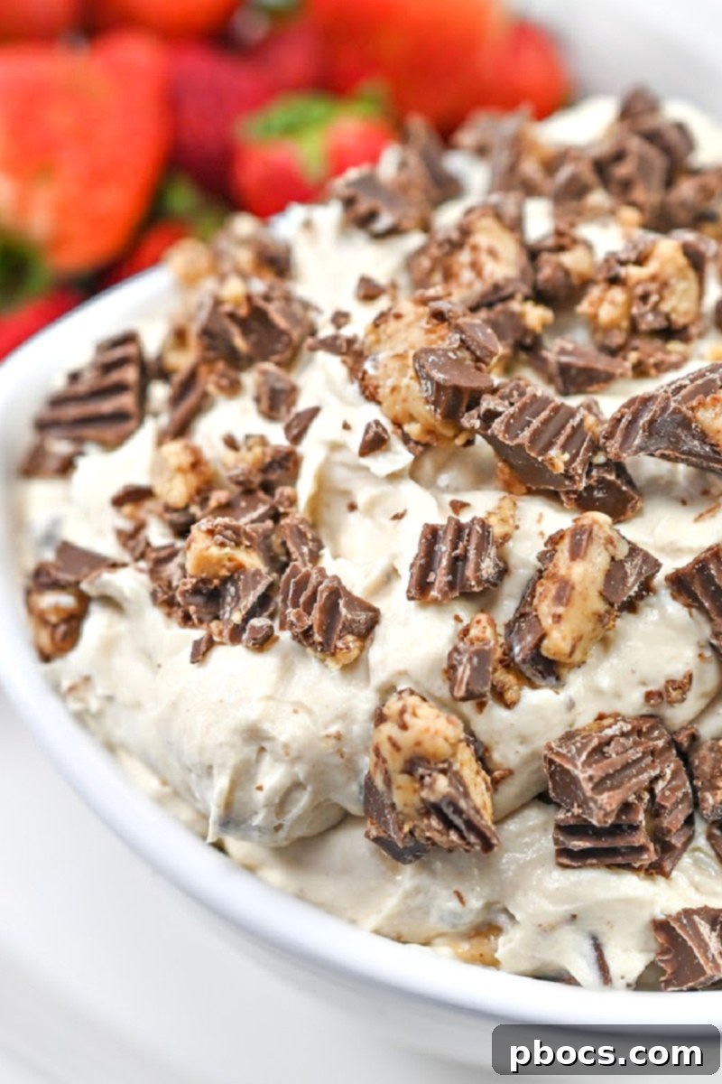Keto Peanut Butter Chocolate Dip 6 Keto Reese's Dip in a white bowl surrounded by an array of keto-friendly dippers, including fresh strawberries and celery sticks
