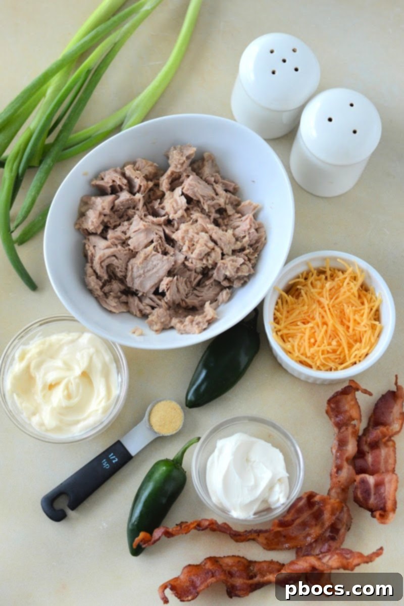 Various fresh ingredients for Keto Jalapeno Popper Tuna Salad neatly arranged on a wooden board: tuna, cream cheese, mayonnaise, jalapenos, cheddar cheese, bacon, garlic powder, and green onions.