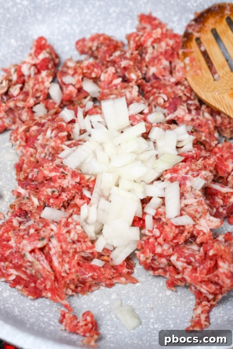 Keto Sausage Lasagna Pinwheels 9 Adding chopped onion to browning Italian sausage in a skillet