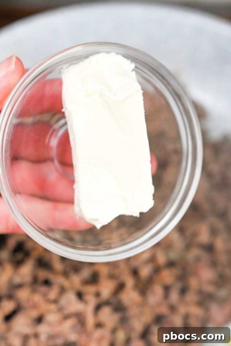 Keto Sausage Lasagna Pinwheels 10 Melted cream cheese being stirred into cooked sausage and onion mixture