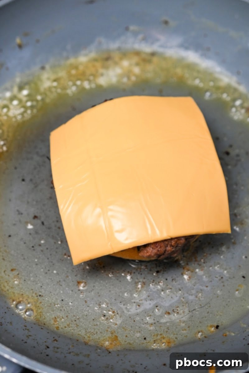 Placing cheese on top of a burger patty resting on a bun in a skillet