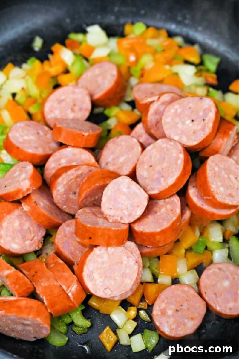 Adding sliced Andouille sausage to the skillet to brown with vegetables.