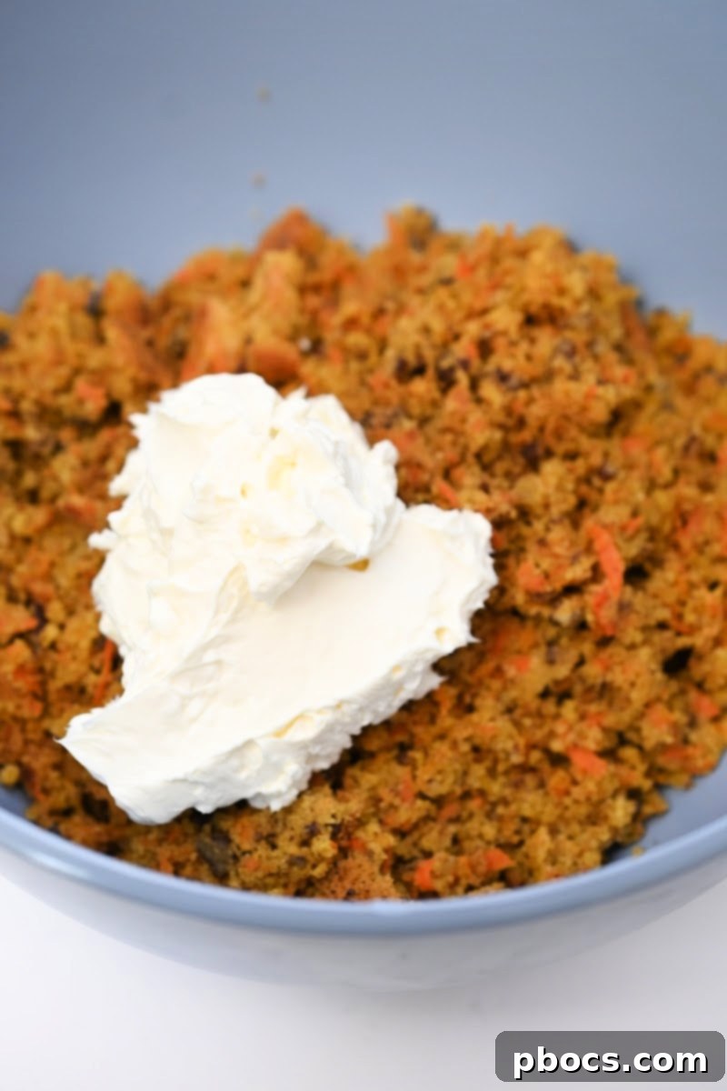 Adding softened cream cheese to the crumbled carrot cake