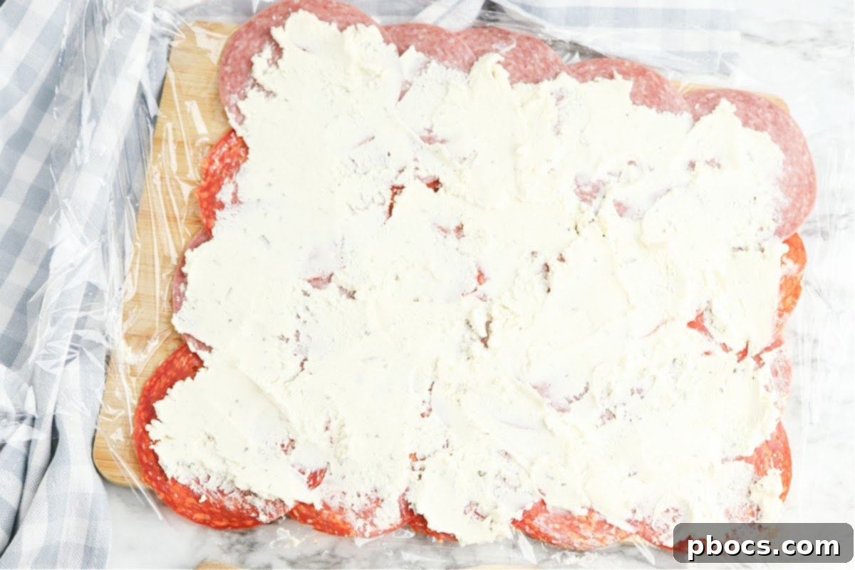 Second step of Keto Boursin Roll Ups: Alternating and overlapping slices of pepperoni and salami on the plastic wrap.