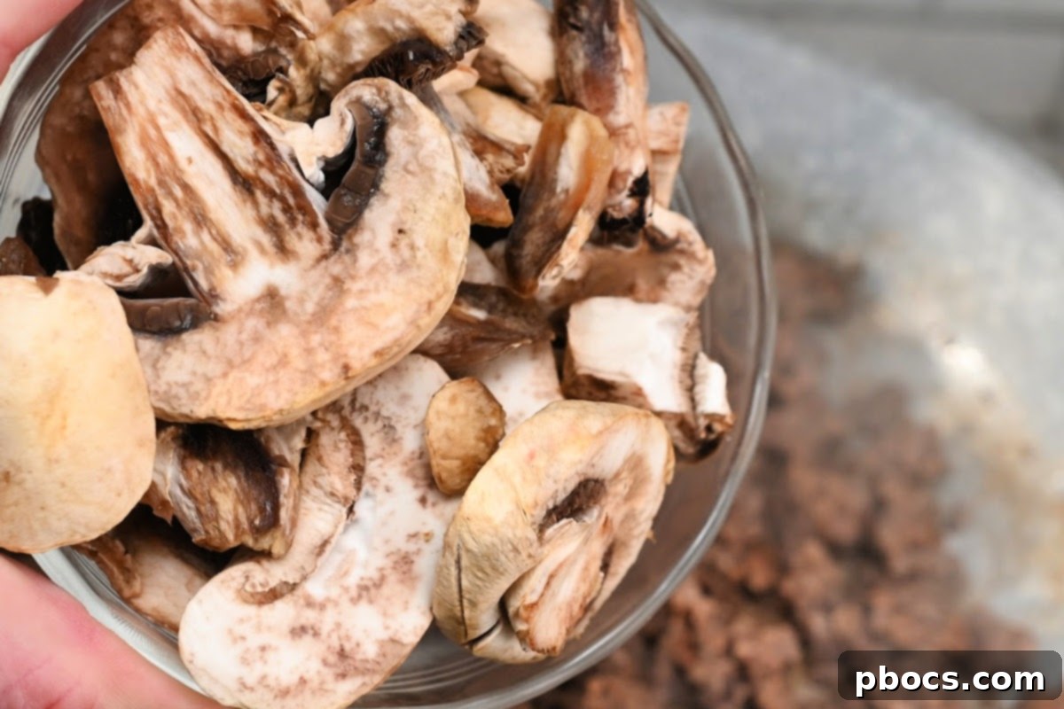 Sliced mushrooms being added to the browned ground beef in a skillet