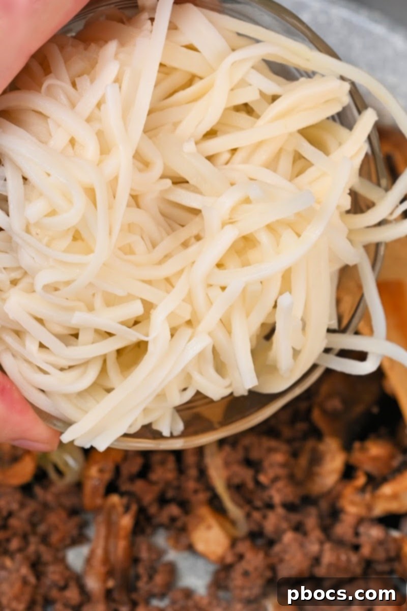 Palmini linguine noodles being added to the skillet with beef and mushrooms