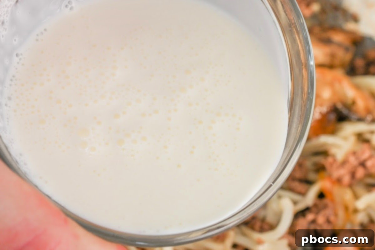 Heavy whipping cream being poured into the French onion pasta skillet