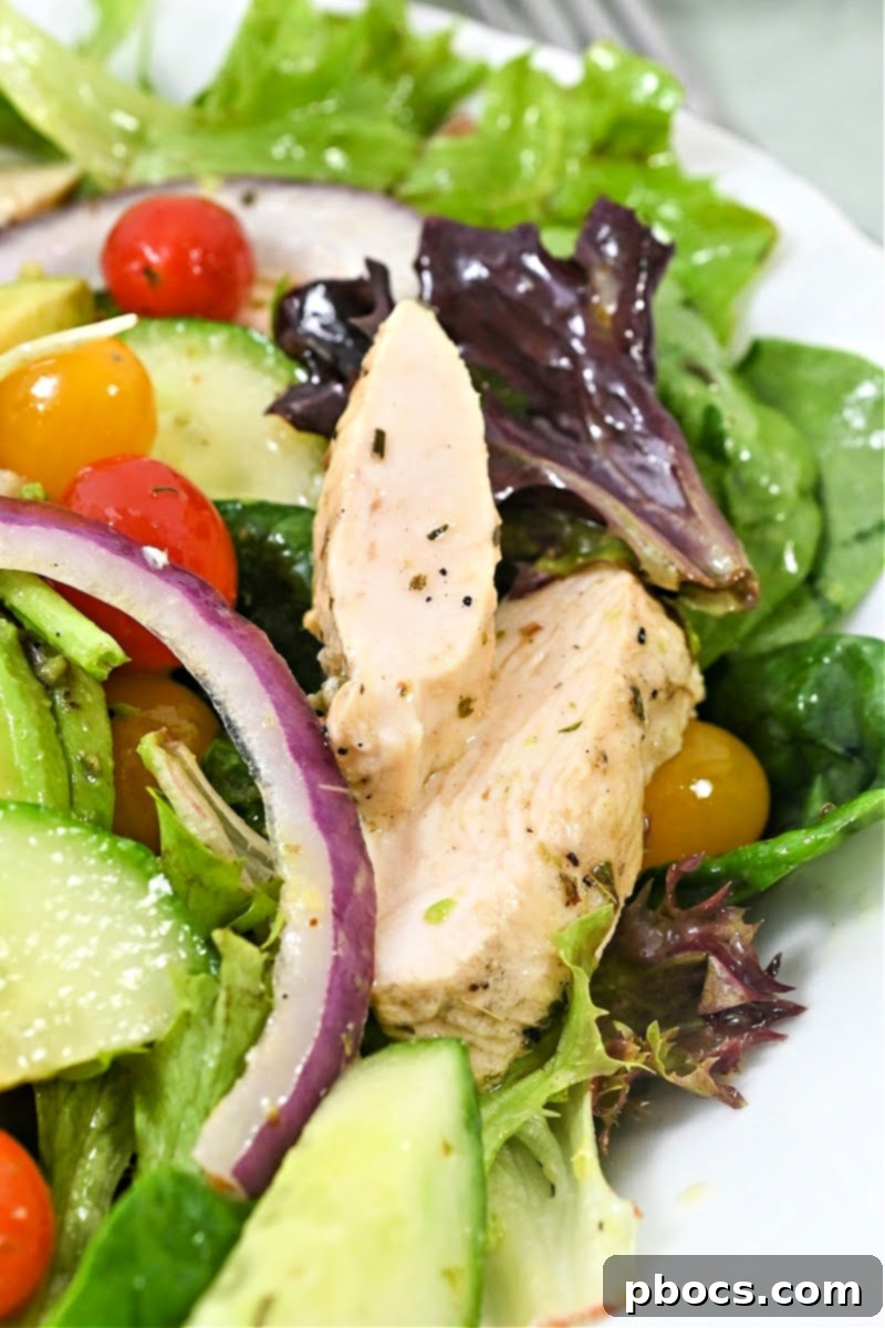 Colorful Keto Lemon Herb Chicken Salad with Avocado - A bowl filled with greens, chicken, tomatoes, cucumber, and avocado.