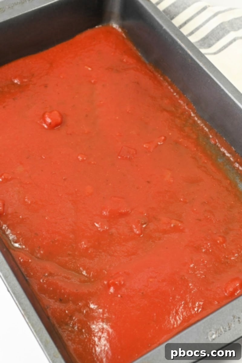 A rectangular baking dish with marinara sauce in the bottom