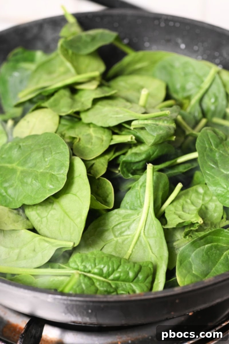 Baby spinach wilting in a skillet with garlic
