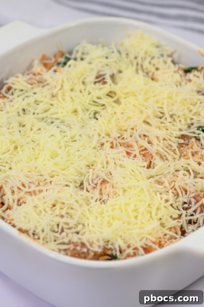Shredded mozzarella cheese being sprinkled over the Keto Cottage Cheese Pasta Bake in a baking dish