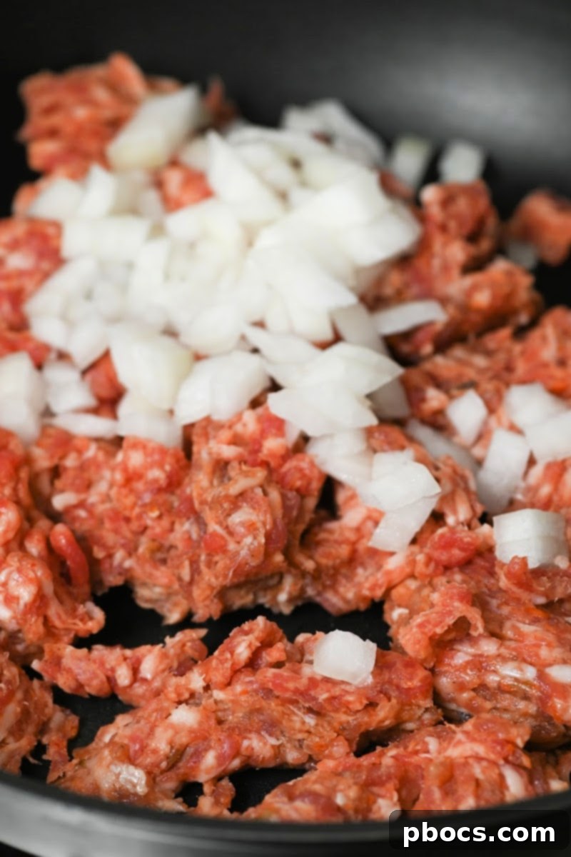 Sausage and chopped onion cooking in a skillet