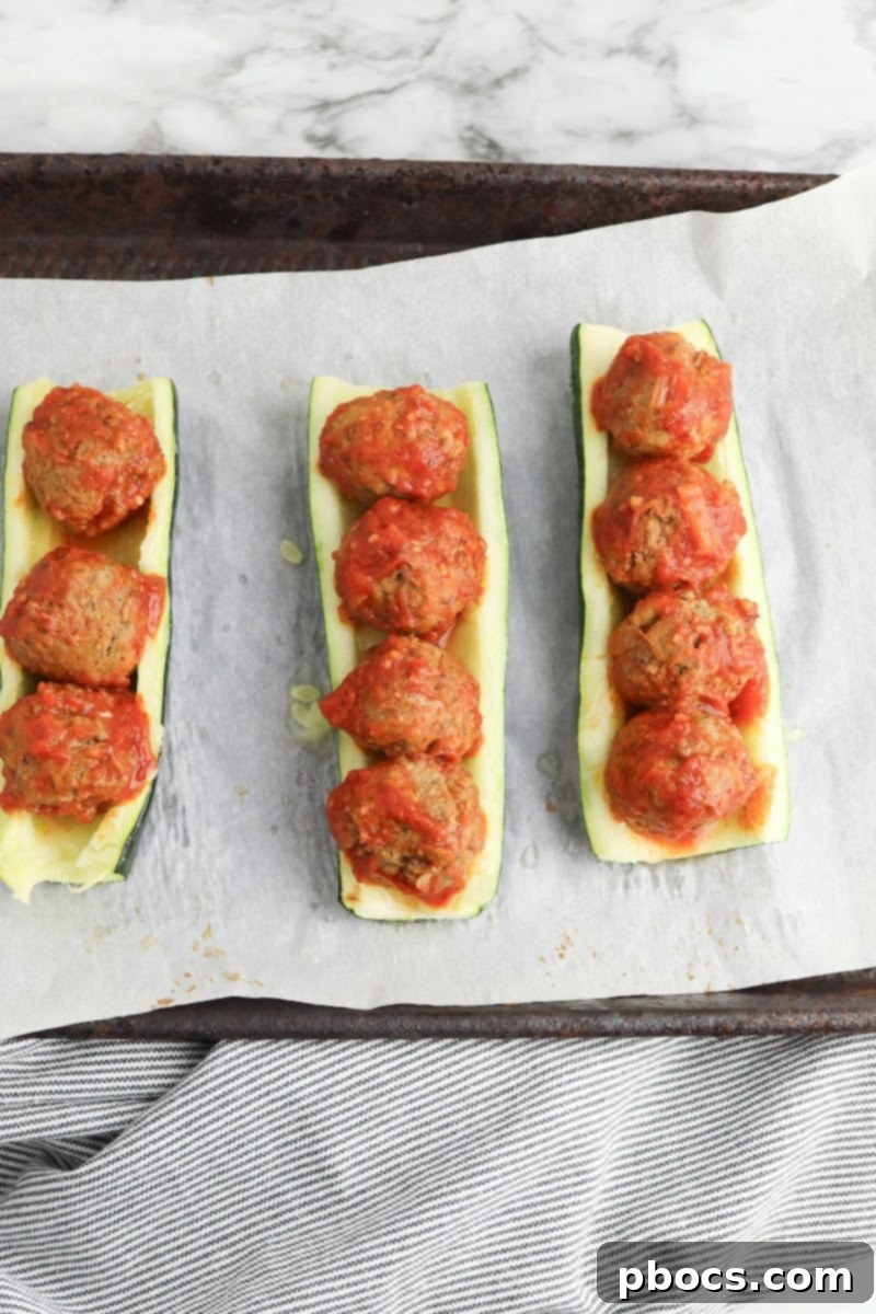 Meatballs on unbaked zucchini boats, ready for cheese