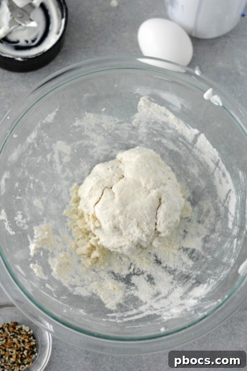 Hands kneading and shaping the bagel dough in a mixing bowl.