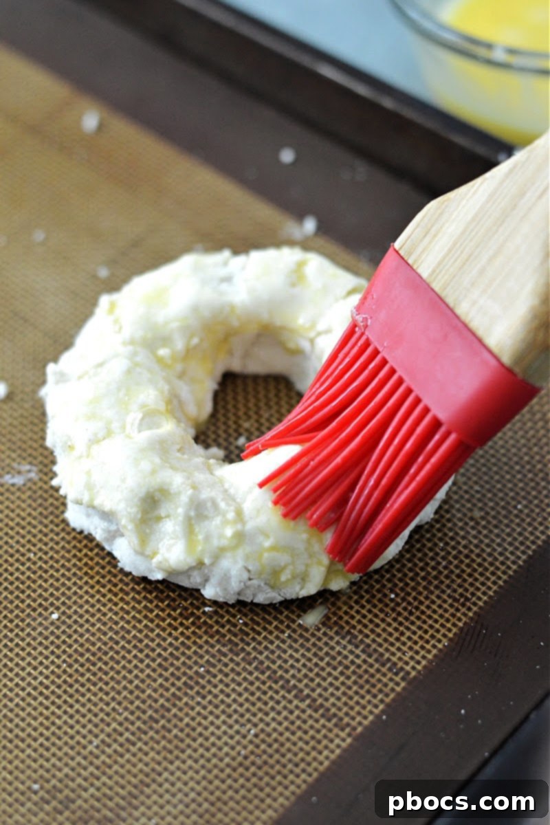 Three shaped bagel doughs on a baking sheet, ready for egg wash.