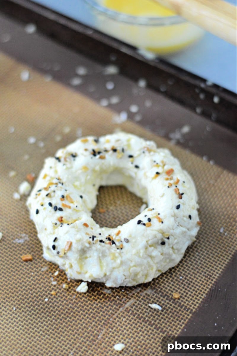 Unbaked keto bagels topped with seasoning on a baking sheet.