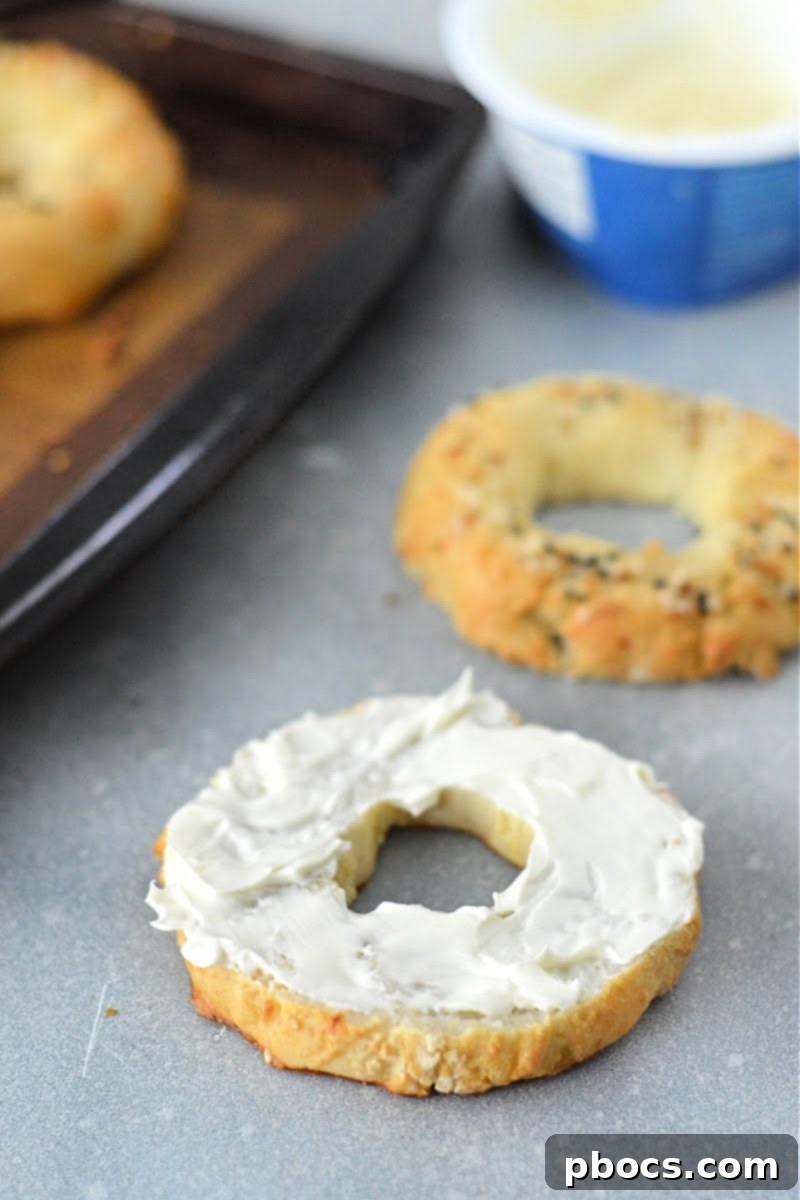Hand spreading cream cheese on a freshly baked Keto Cottage Cheese Bagel, highlighting its soft interior.