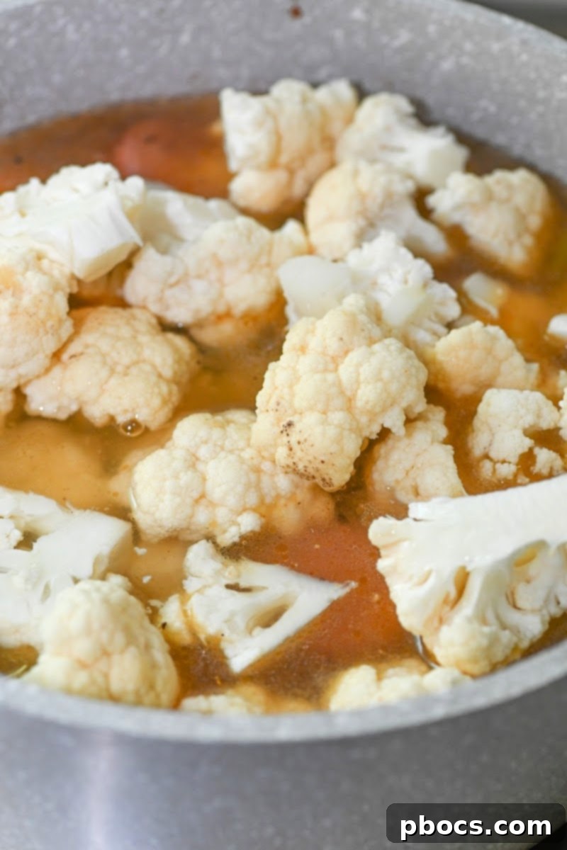 Cauliflower florets being added to the simmering soup base in a pot
