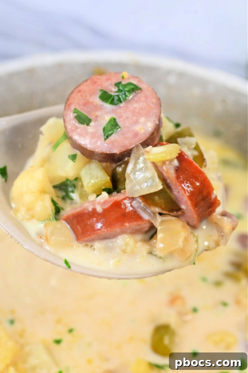 Close-up of a steaming bowl of Keto Creamy Kielbasa and Cauliflower Soup, showing chunks of sausage and cauliflower
