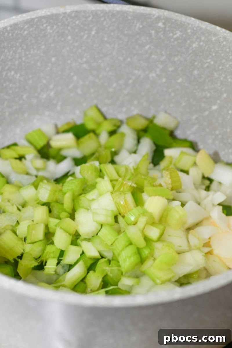 Diced onions, green bell peppers, and celery sautéing in butter in a large pot