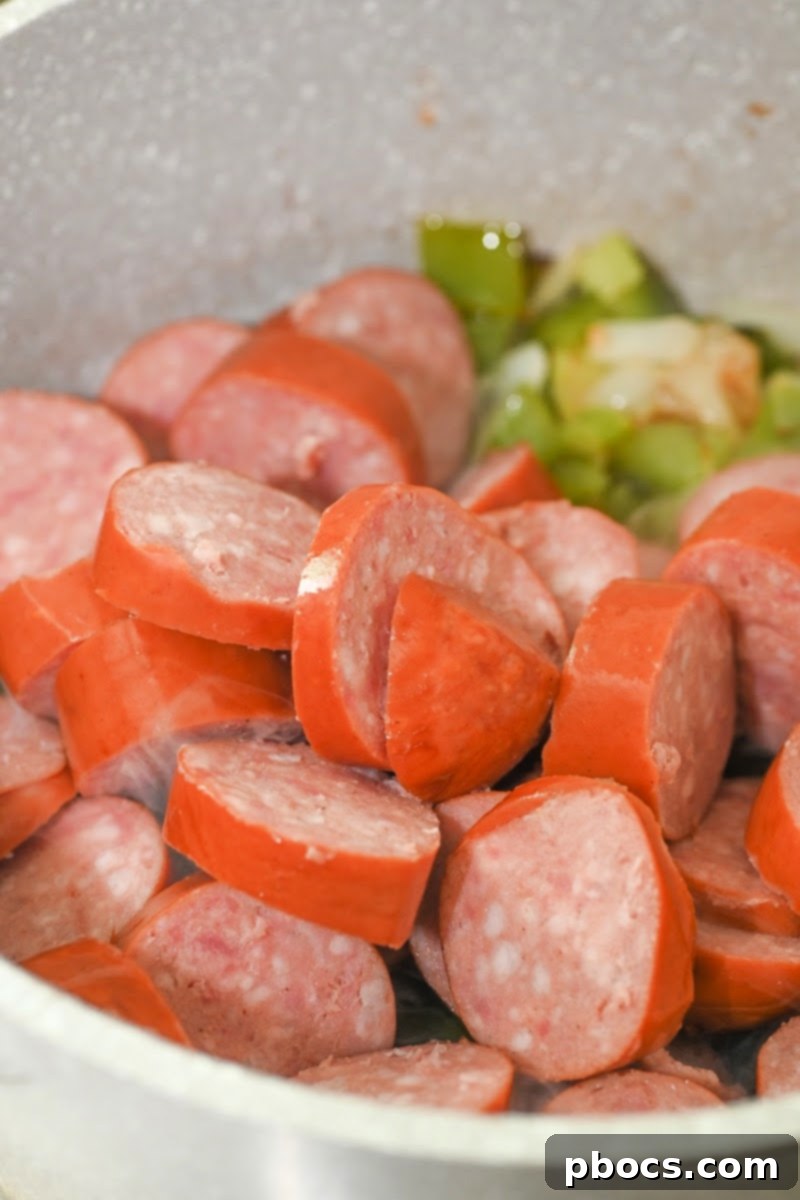Sliced kielbasa sausages being sautéed in a pot with vegetables