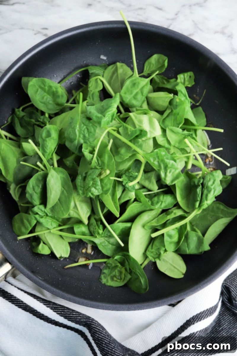 Mediterranean Keto Spinach Feta Bake 12 Spinach wilting in a skillet.