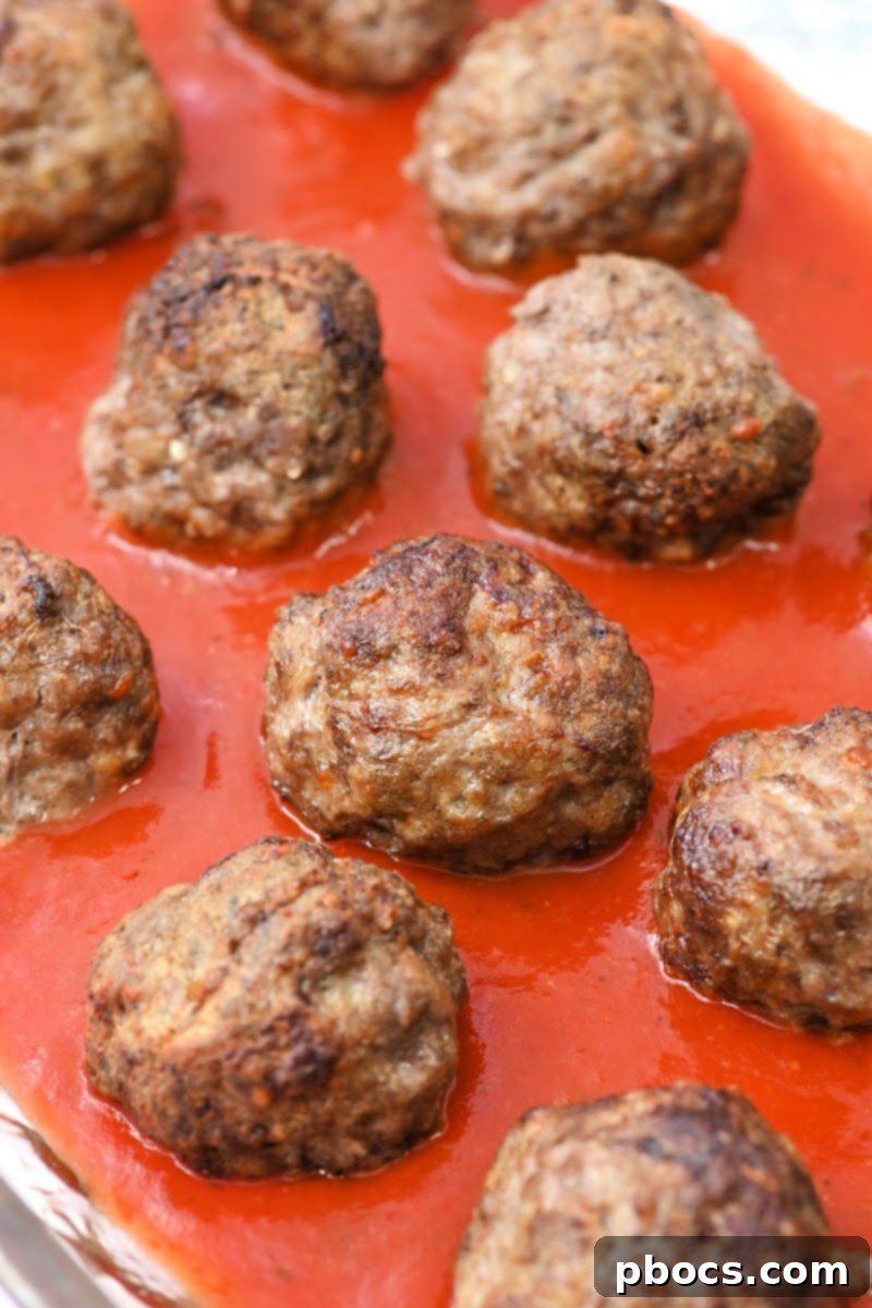 Cooked meatballs nestled in a 9x13 baking dish with marinara sauce