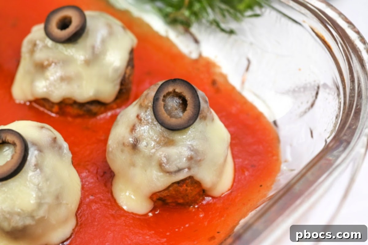 Keto Meatball Eyeballs with melted cheese and black olive irises in a baking dish