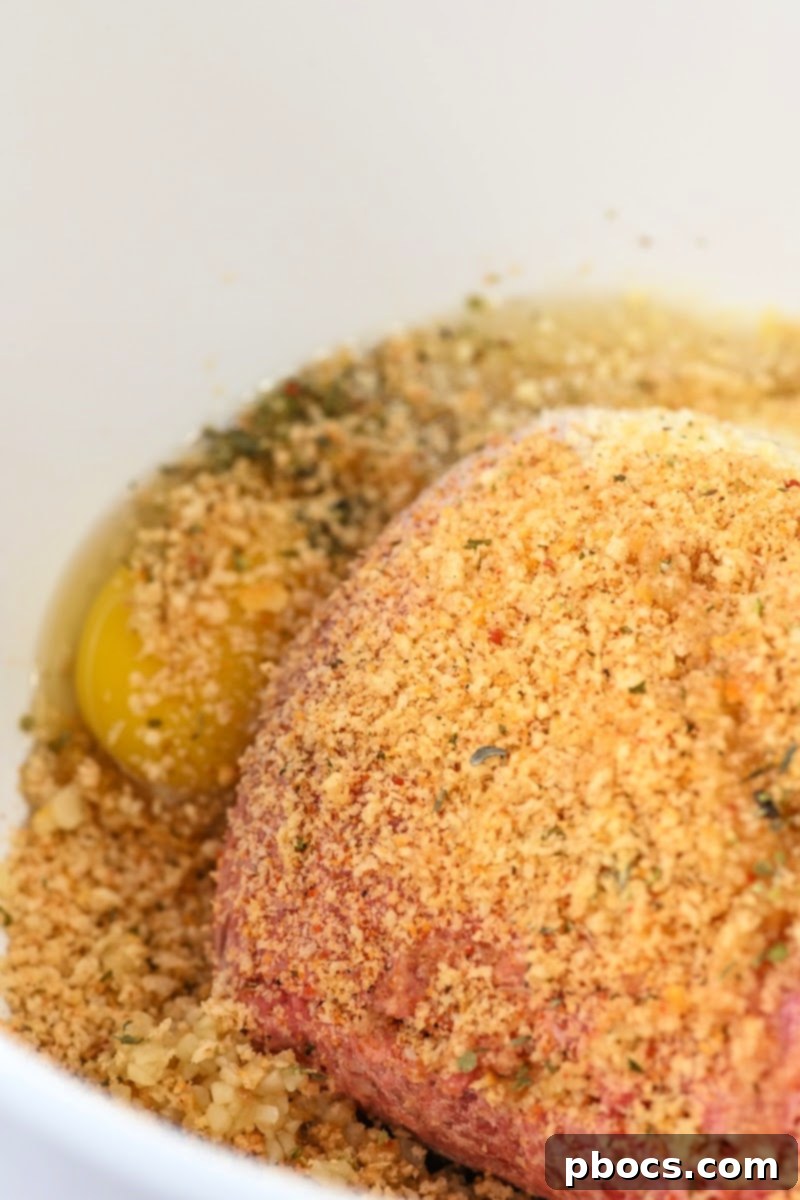 Mixing ground beef, egg, parmesan, pork rinds, garlic, and seasoning in a bowl