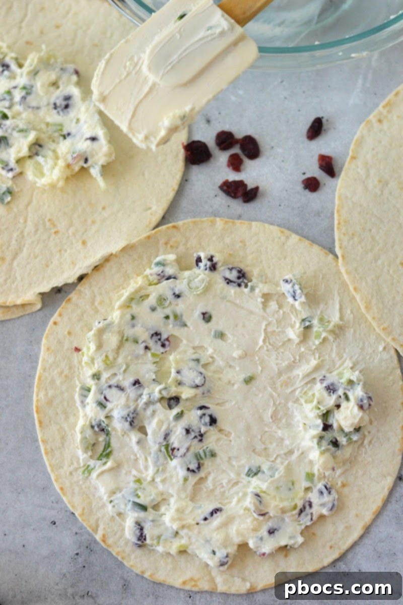 A tortilla with cream cheese mixture spread across, ready to be rolled up.