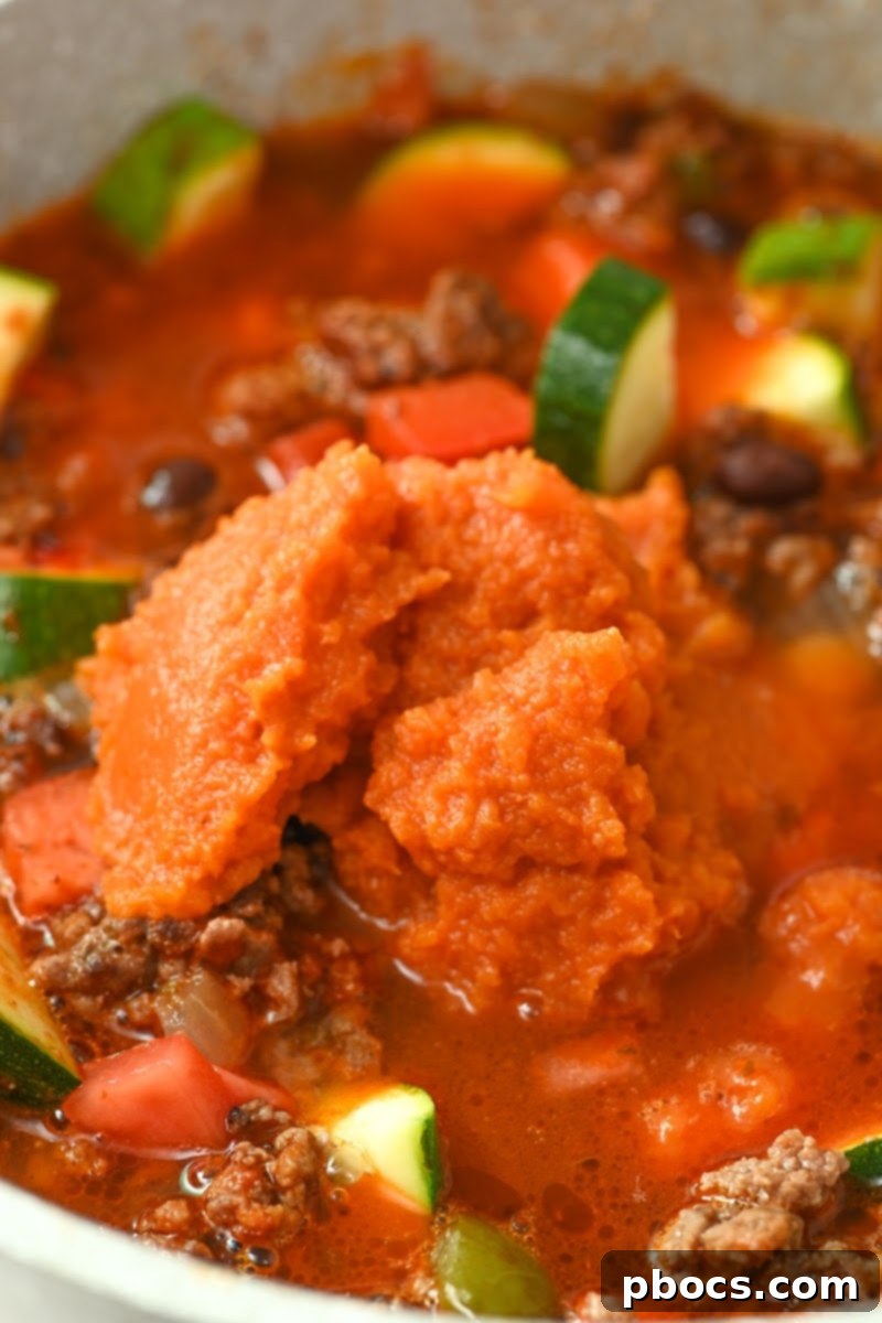 Adding pumpkin puree to the simmering chili