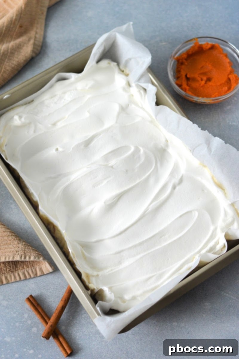 Spreading caramel-infused whipped topping over the warm poke cake