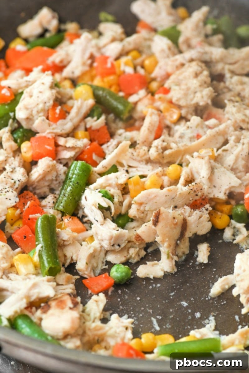 Adding shredded chicken and mixed vegetables to a skillet with melted butter.