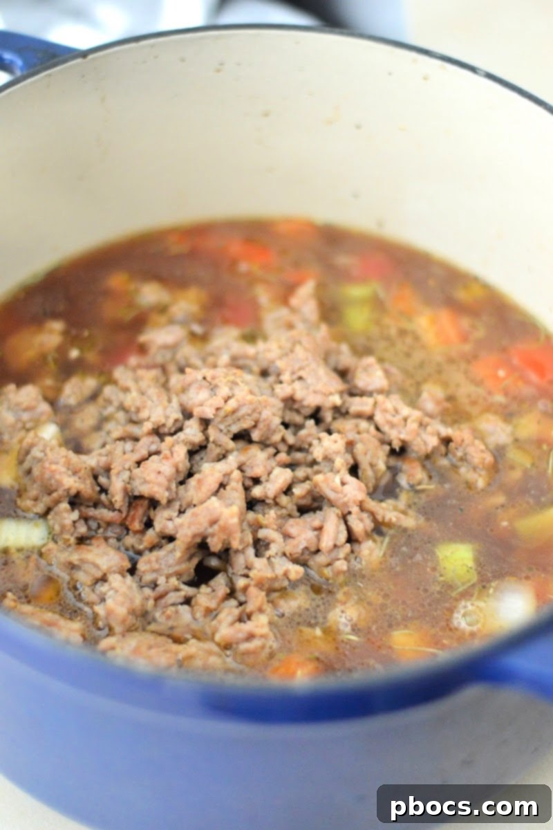 Cooked sausage and beef broth being added to the vegetable mixture in a pot