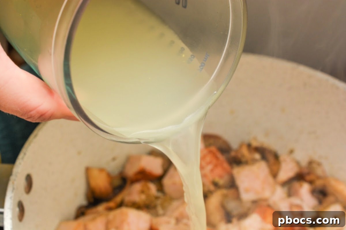 Adding chicken broth to the creamy mushroom sauce