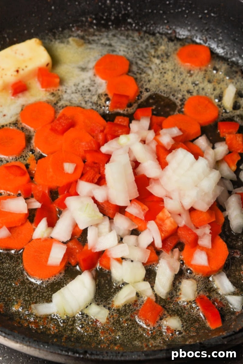 Onions, carrots, and red bell peppers sautéing in butter in a skillet