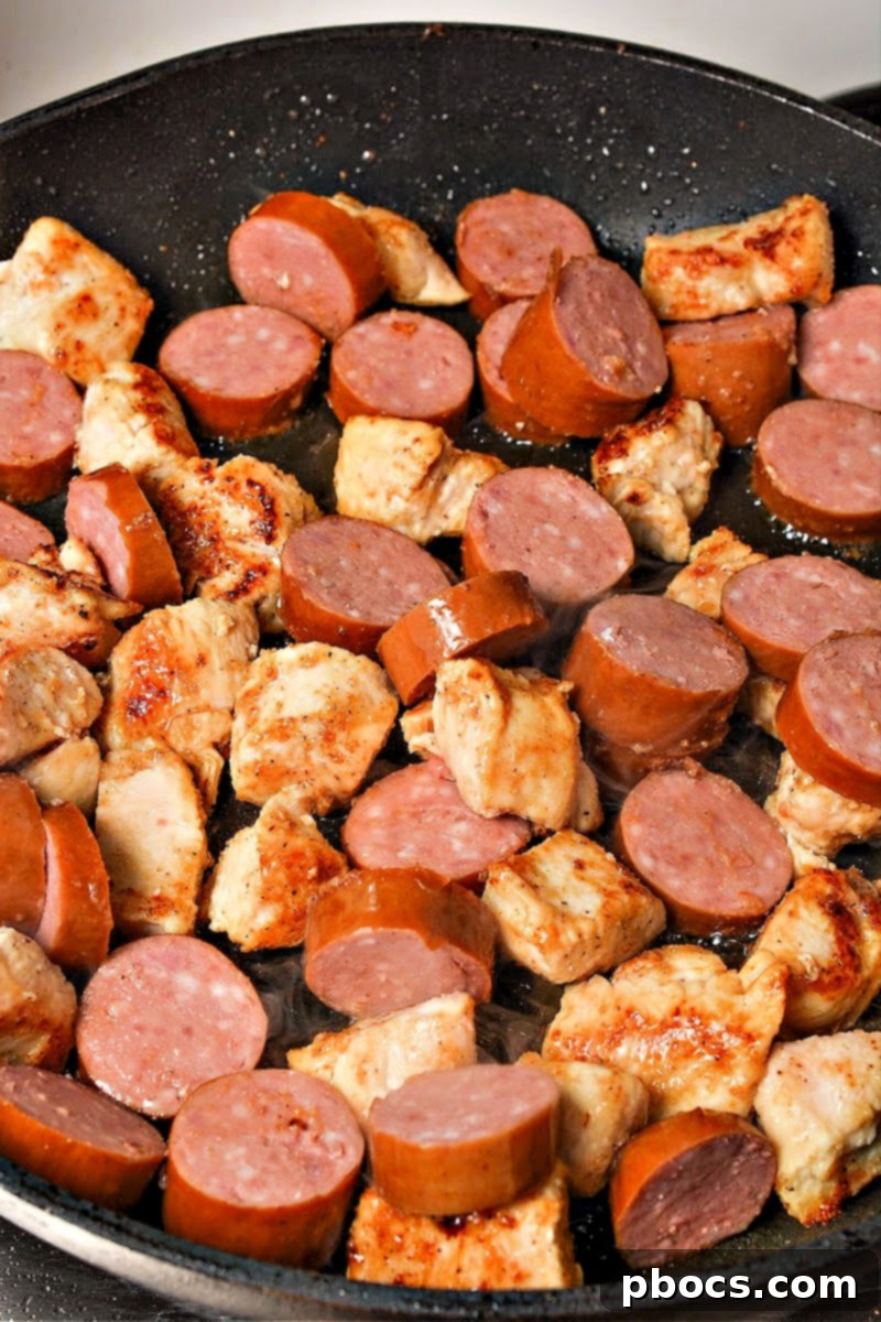 Sausage slices added to seared chicken in a skillet