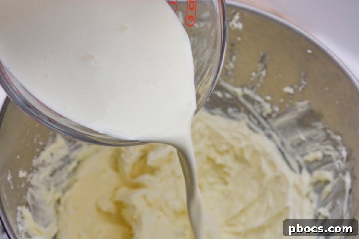 Heavy cream being poured into the cheesecake mixture in a mixing bowl