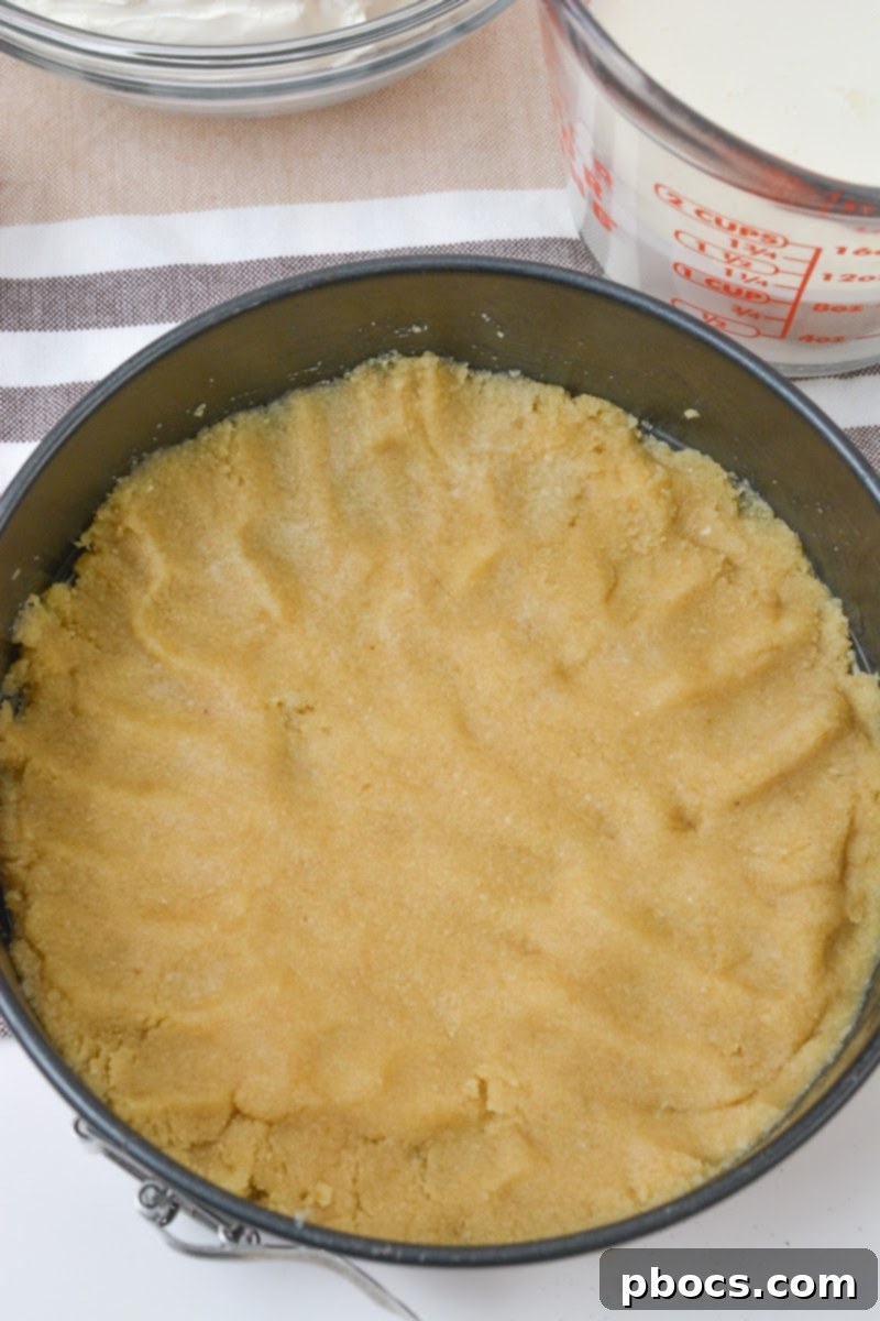 Hands pressing the cheesecake crust mixture into the bottom of a springform pan