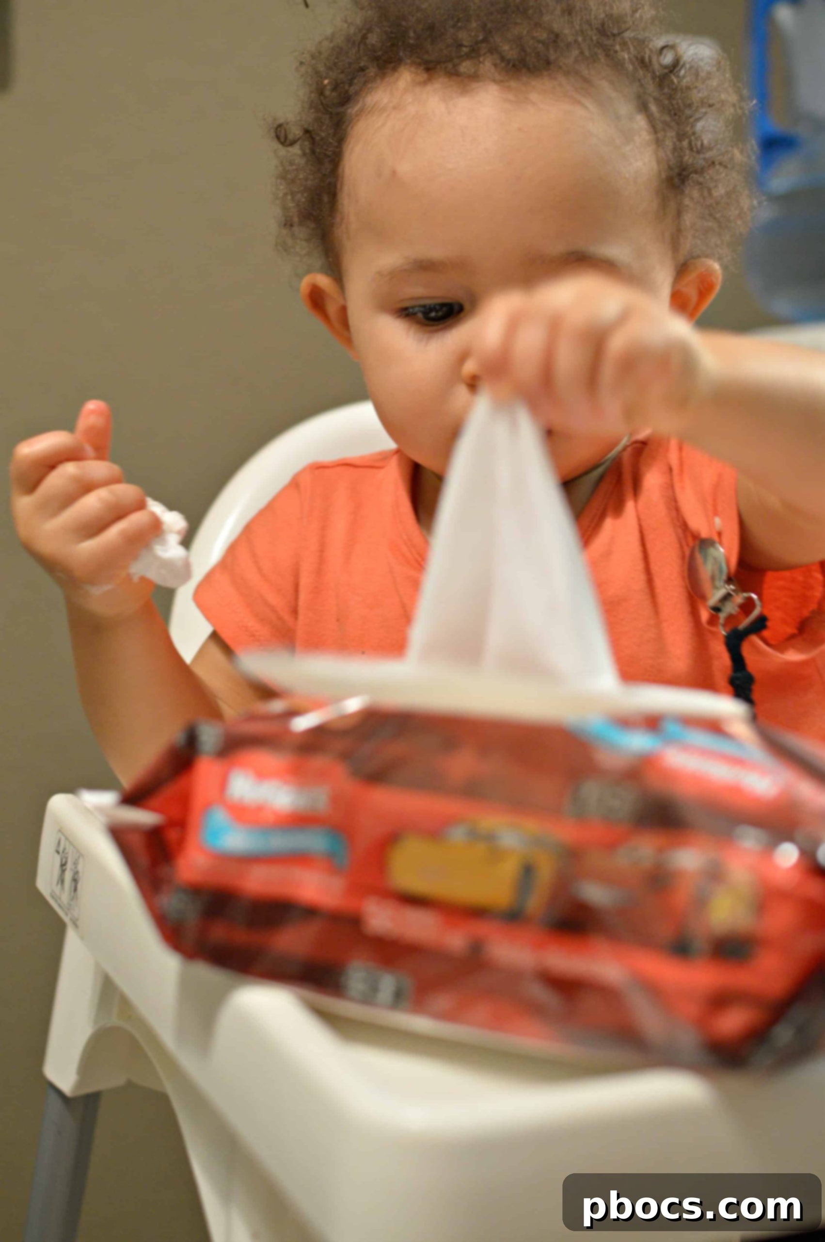 A parent assisting a toddler who is learning to self-feed, with wipes ready for cleanup.