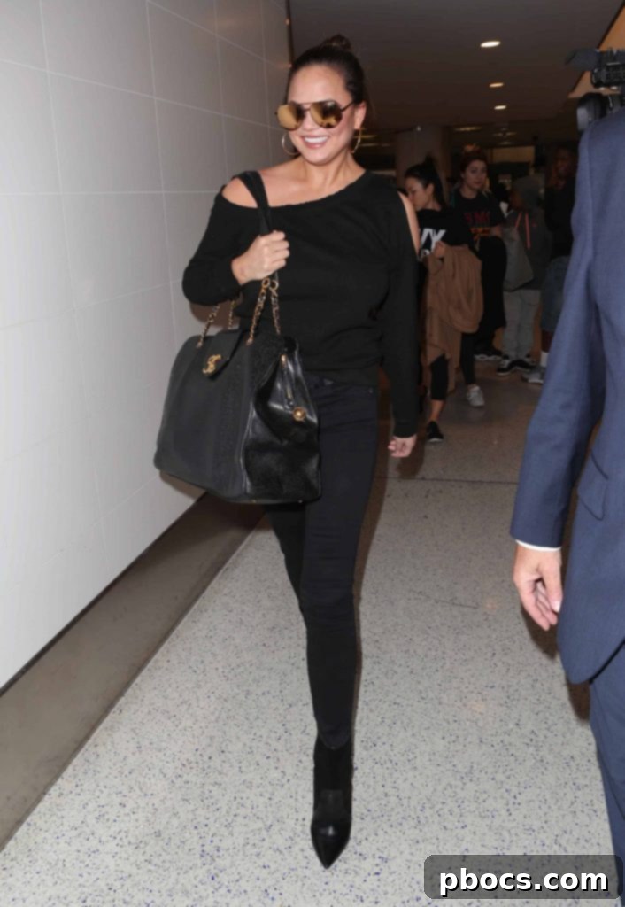 Chrissy Teigen effortlessly rocks a cold shoulder sweater with black jeans and booties.